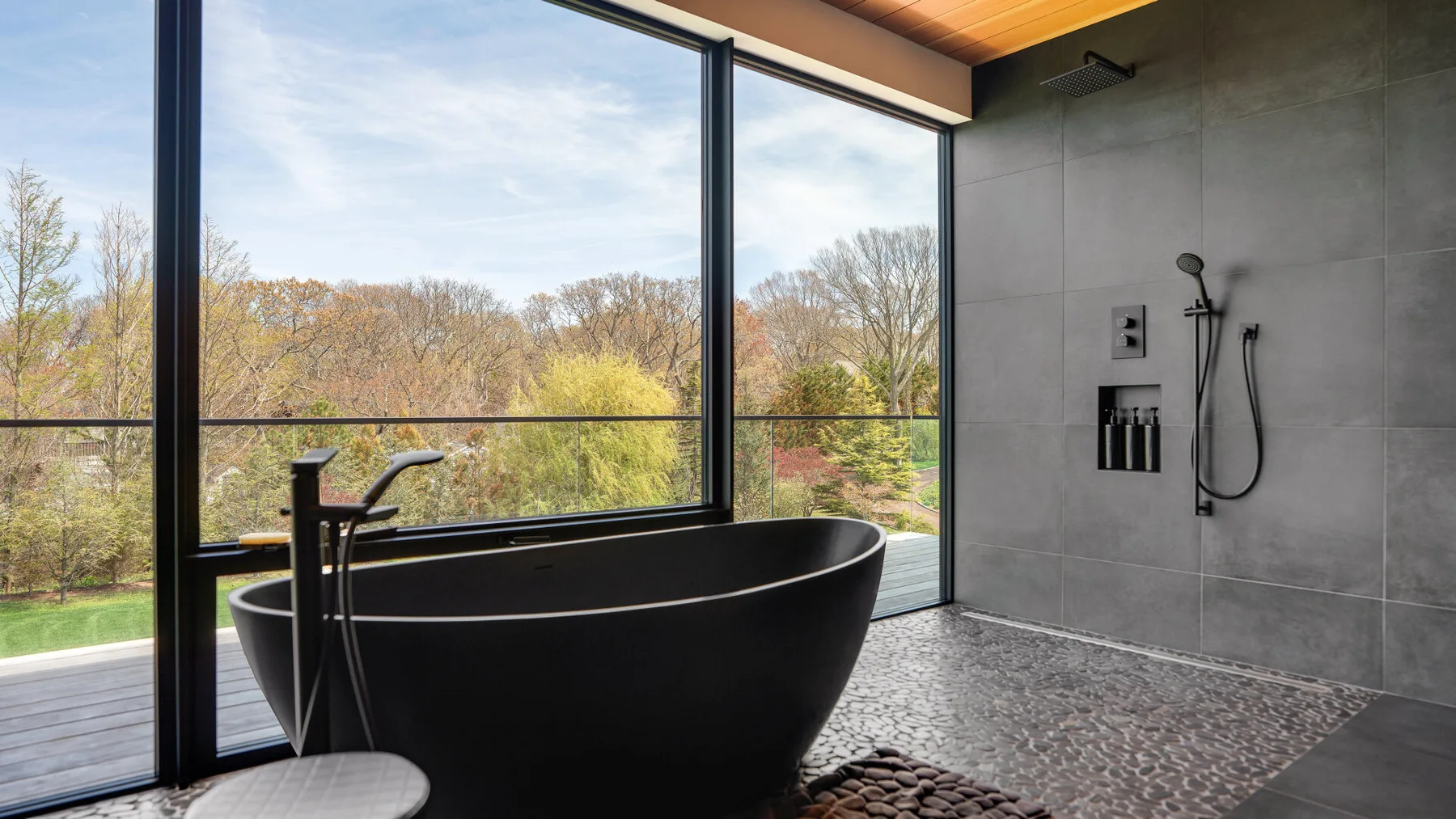 A modern bathroom with a freestanding bathtub beside large windows overlooking trees.