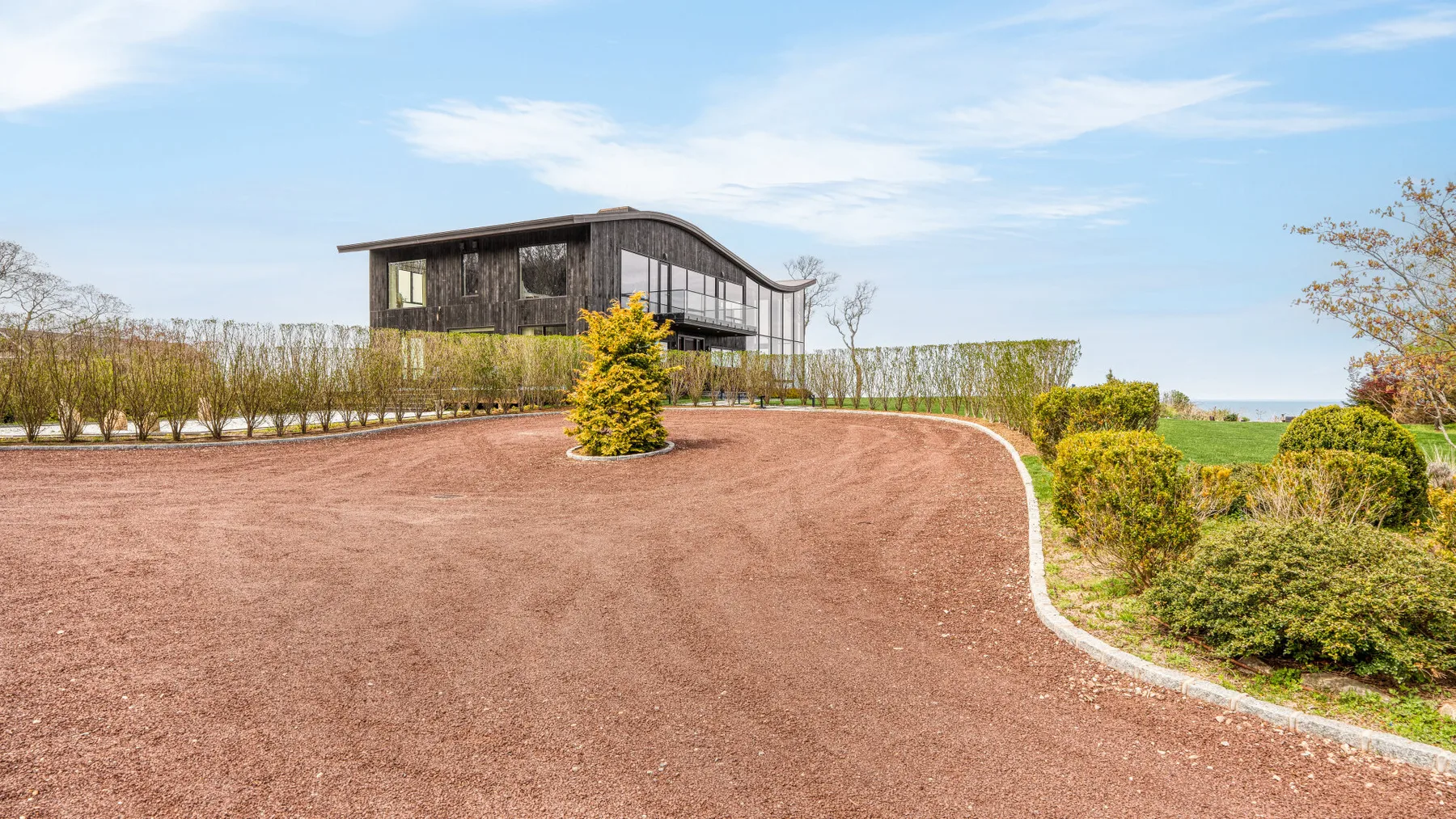 A modern dark-sided house stands beyond a wide curved gravel driveway.