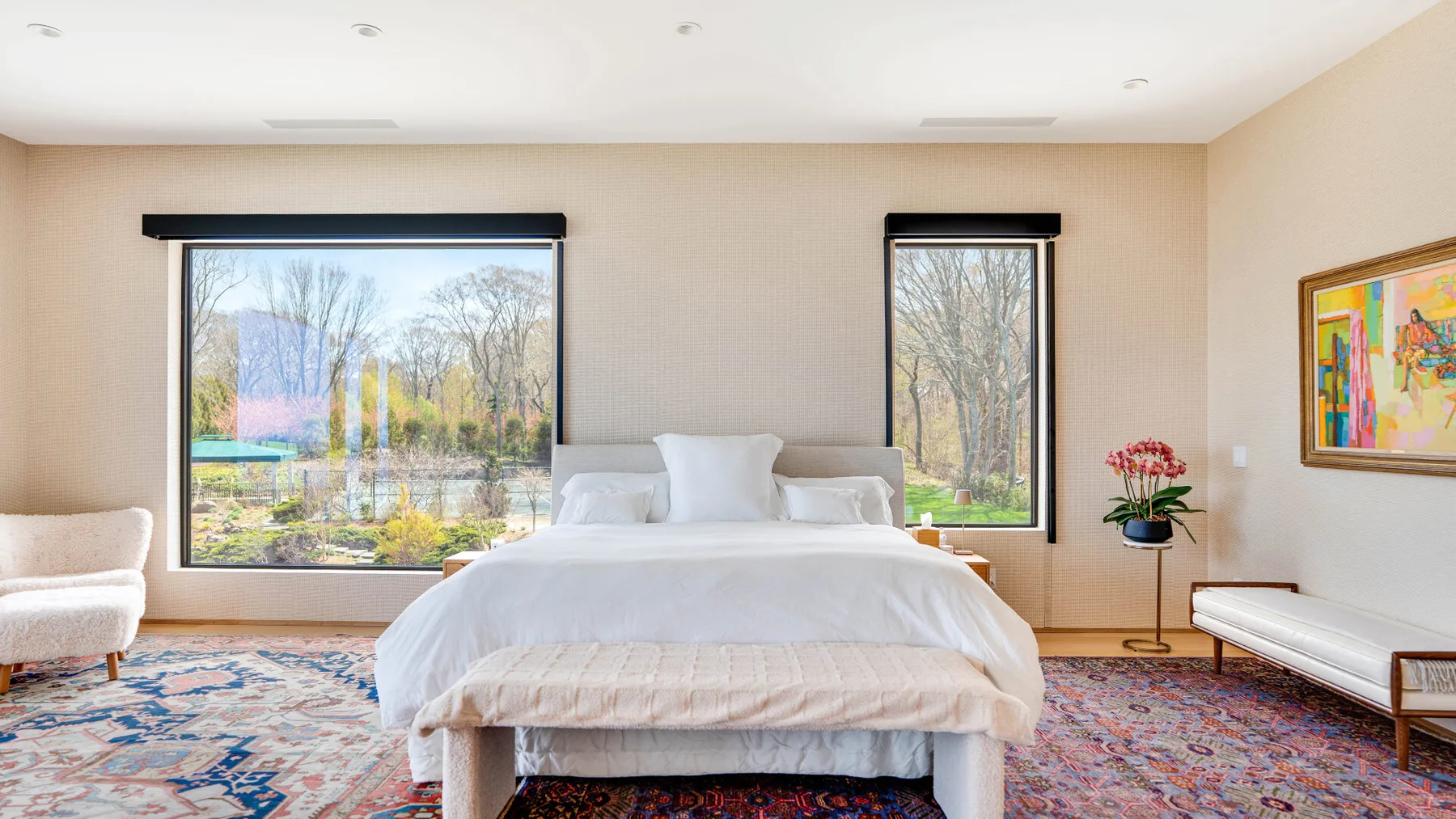A bright bedroom with a bed between two large windows and a colorful rug.