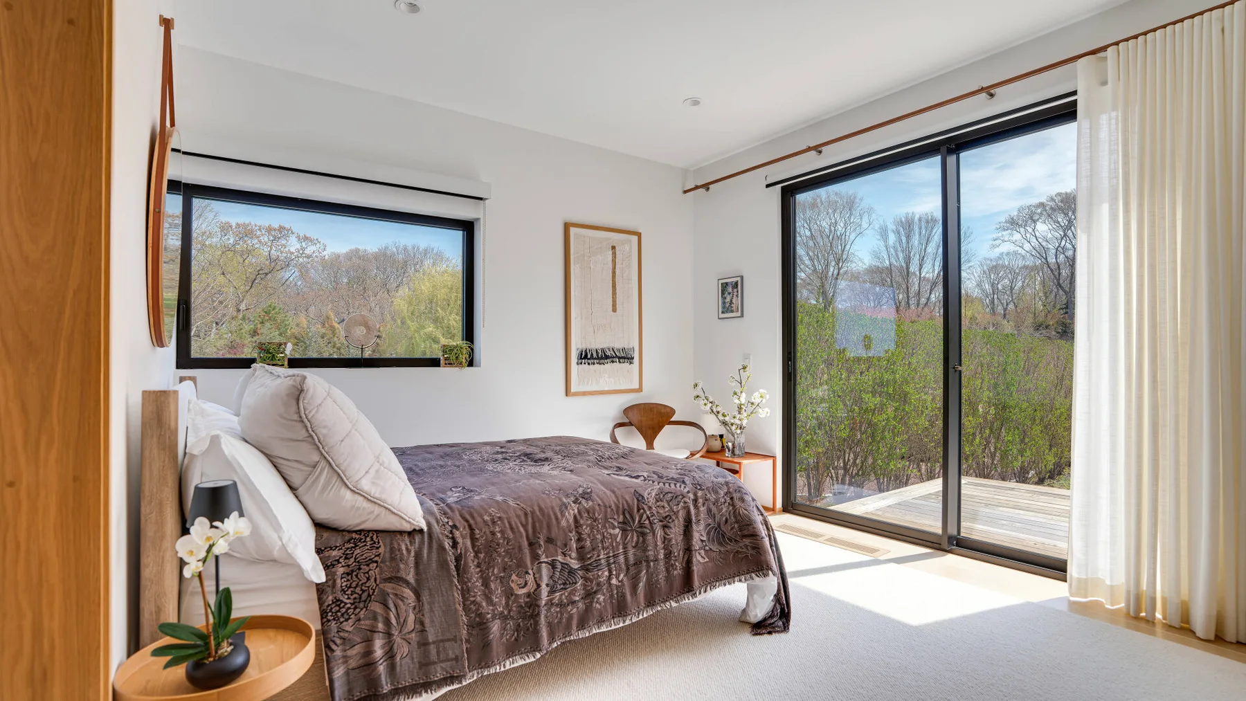 A bedroom with a bed beside large windows overlooking trees and greenery.