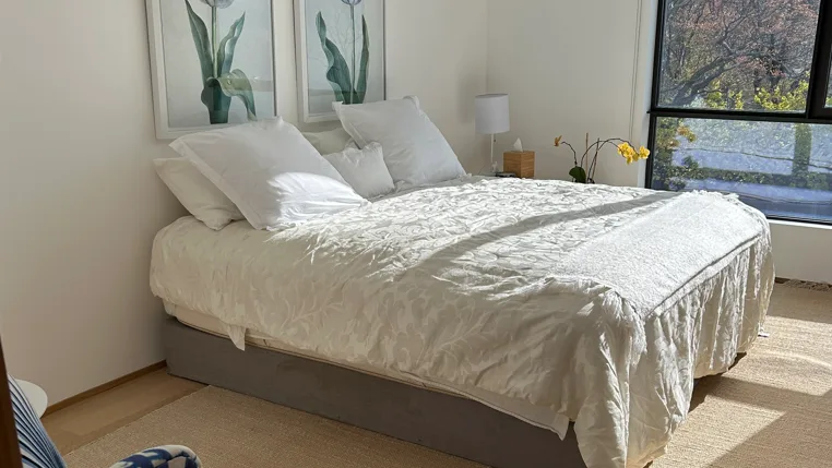 A bright bedroom with a neatly made bed and botanical prints above it.