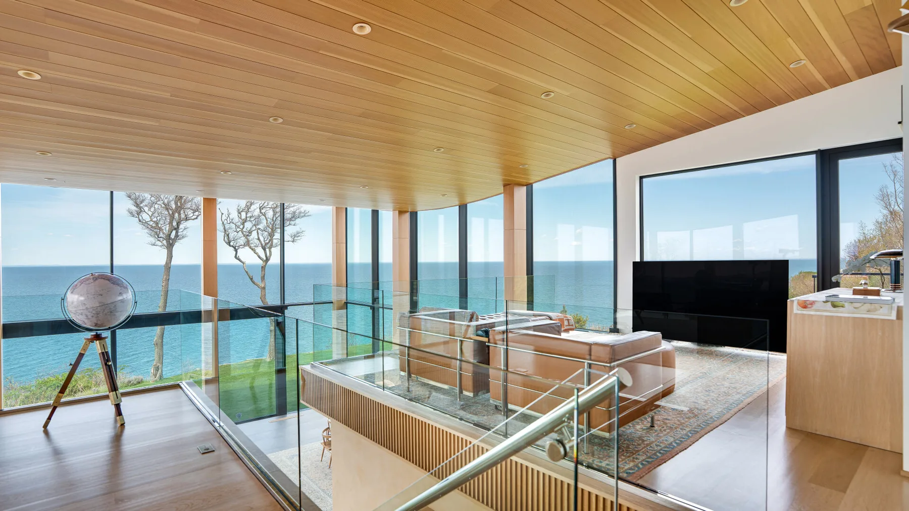 A modern living room with seating and glass walls overlooking the sea.