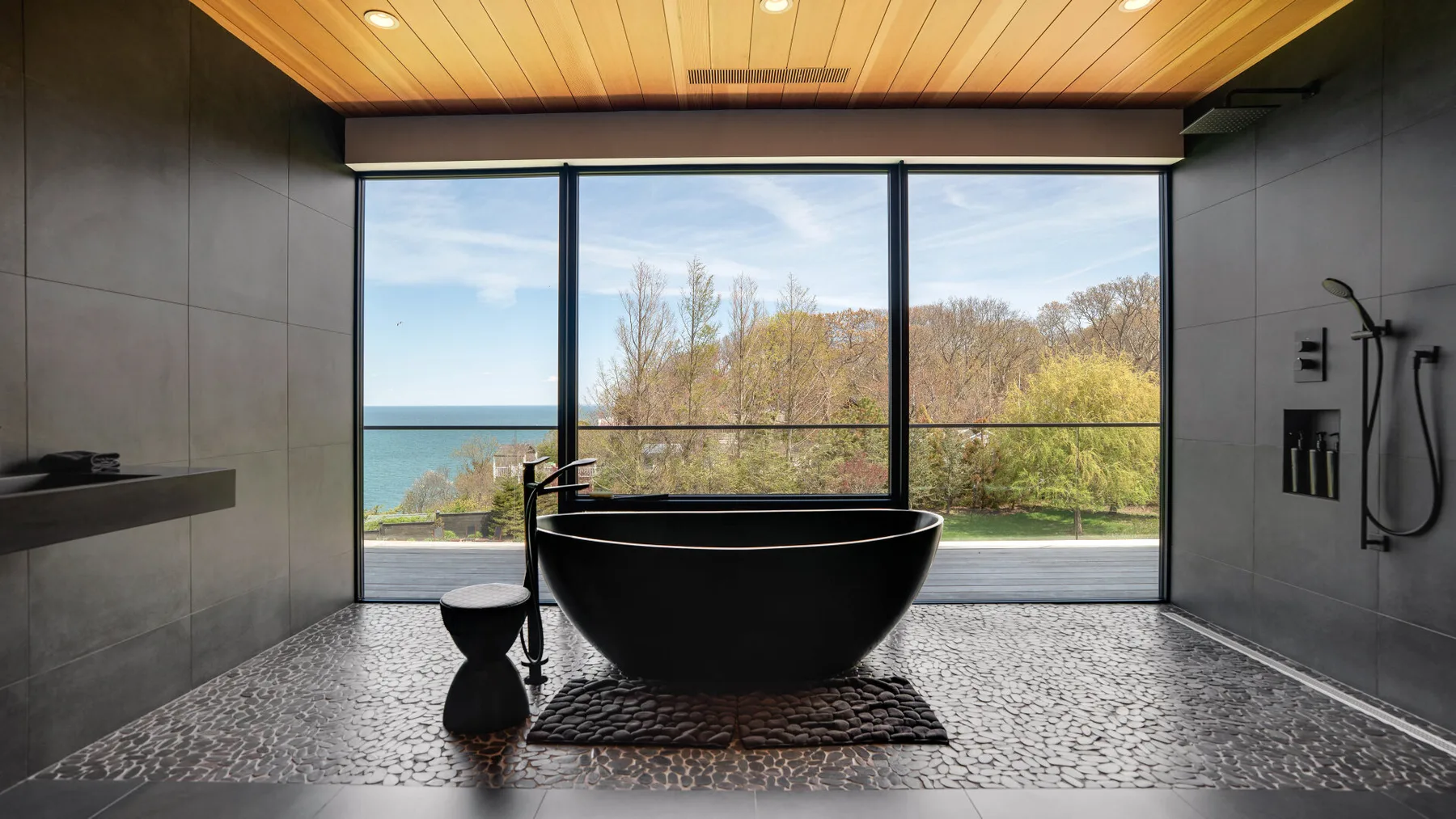 A freestanding bathtub sits before broad windows overlooking trees and water.