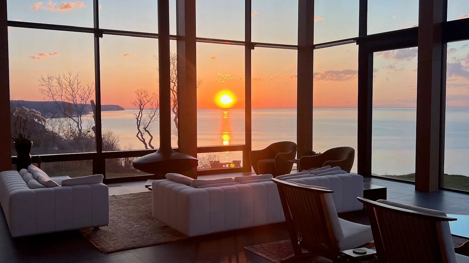 A living room with seating beside floor-to-ceiling windows overlooking the sunset.