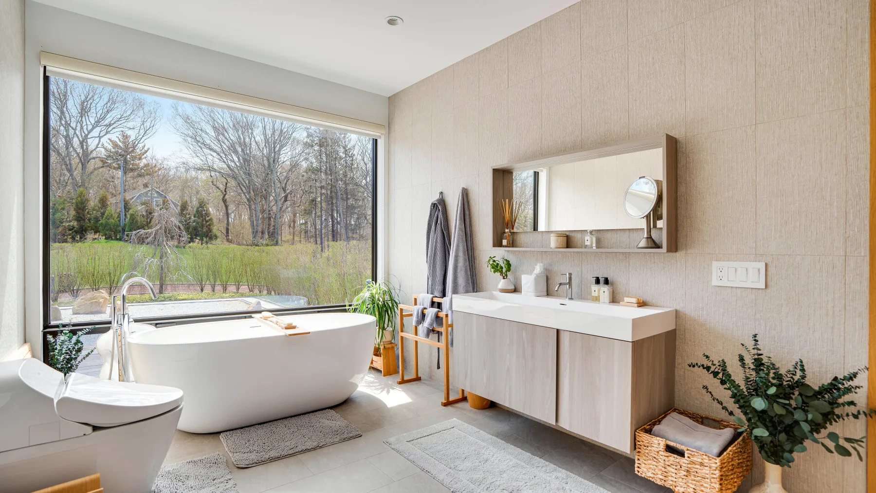 A bright bathroom features a freestanding bathtub beside a large window.