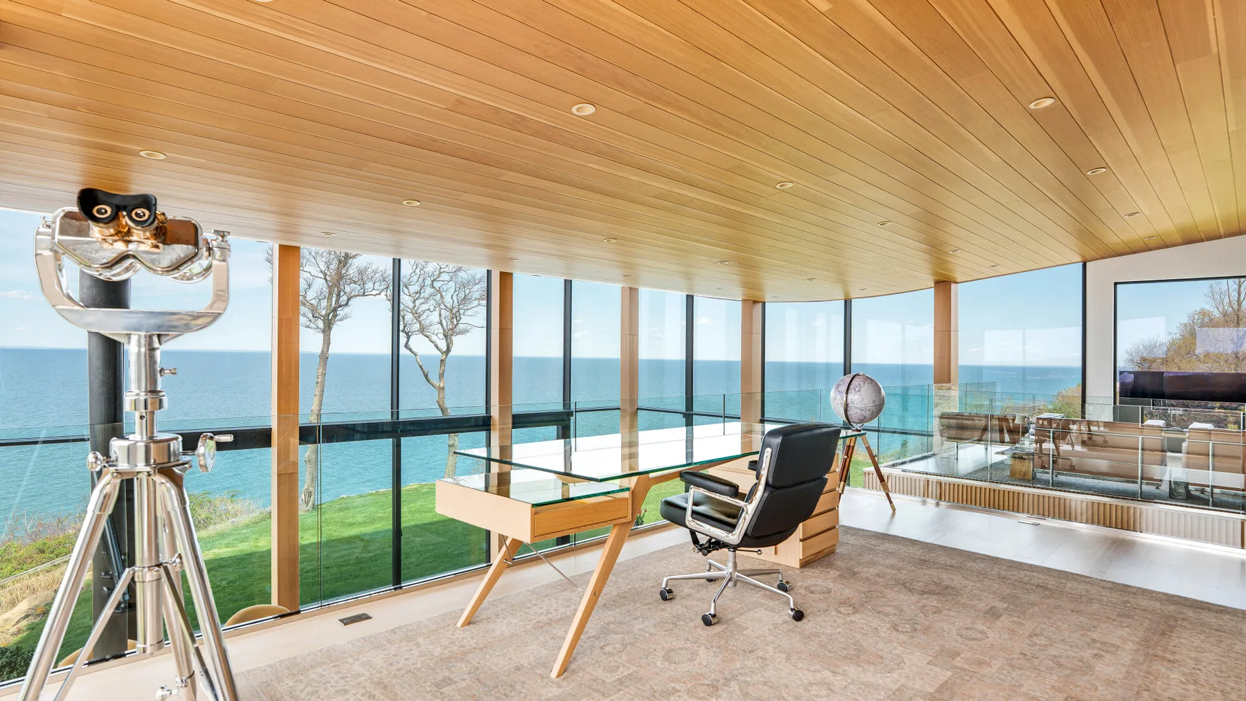 A bright room with floor-to-ceiling windows overlooking the water and a desk with seating.