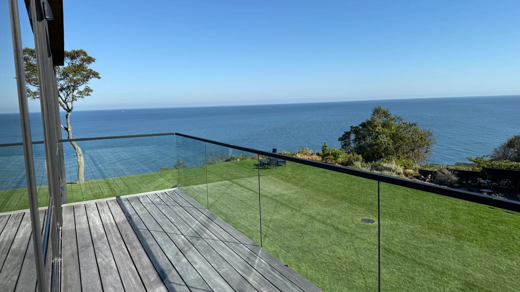 A deck and lawn overlook the ocean behind a glass railing.