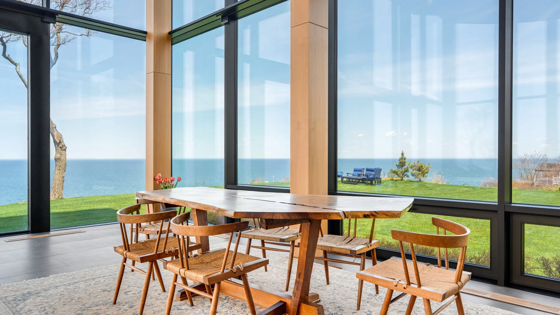 A dining table with wooden seating sits beside large windows overlooking the sea.