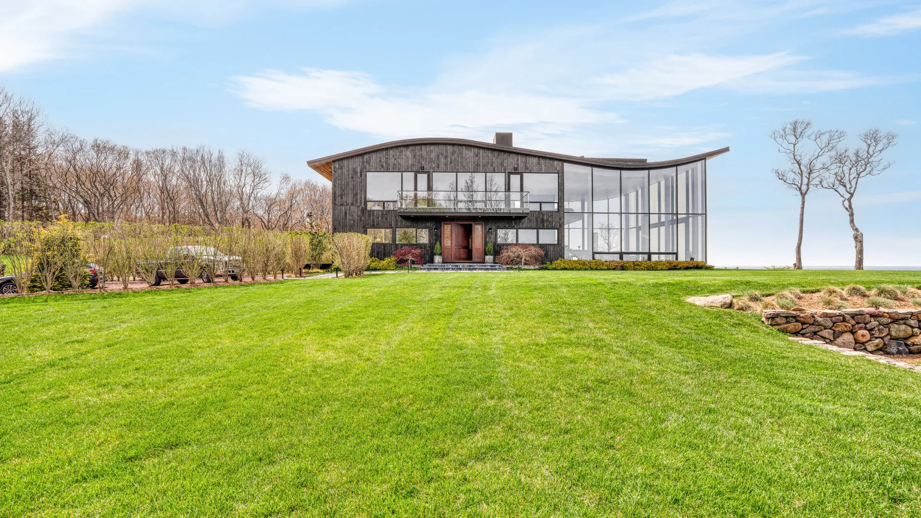 A modern glass-fronted house stands beyond a broad green lawn.