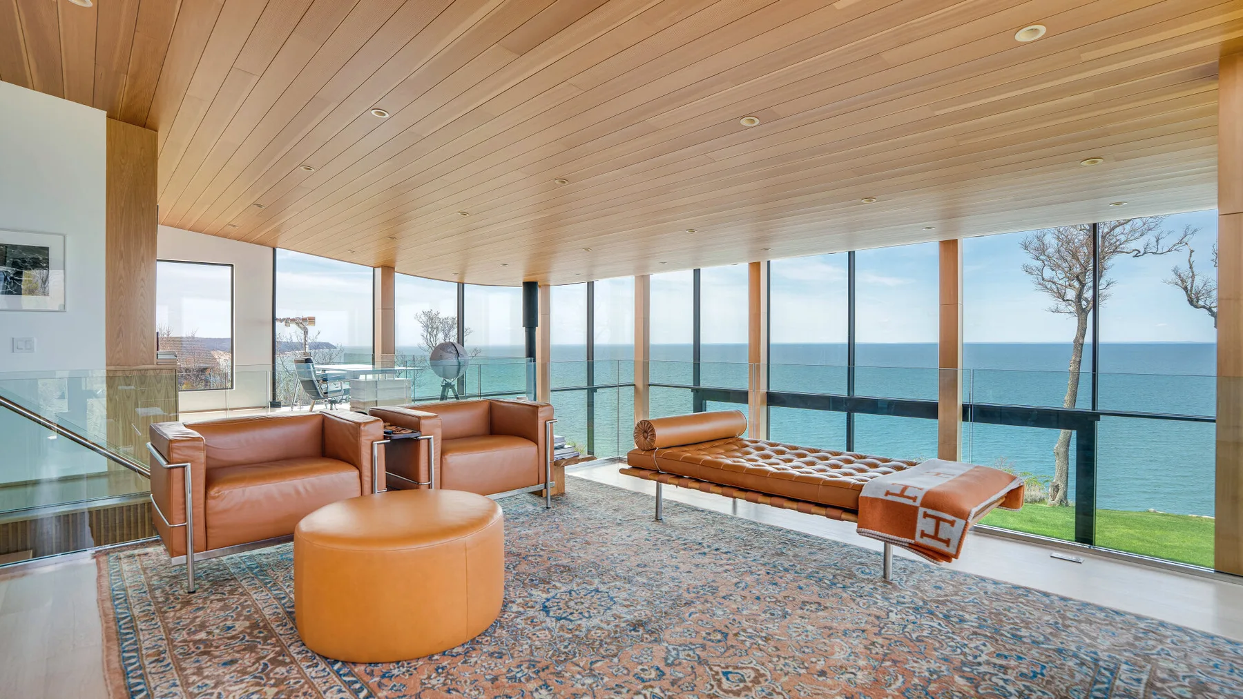 A bright living room with seating beside floor-to-ceiling windows overlooking the water.