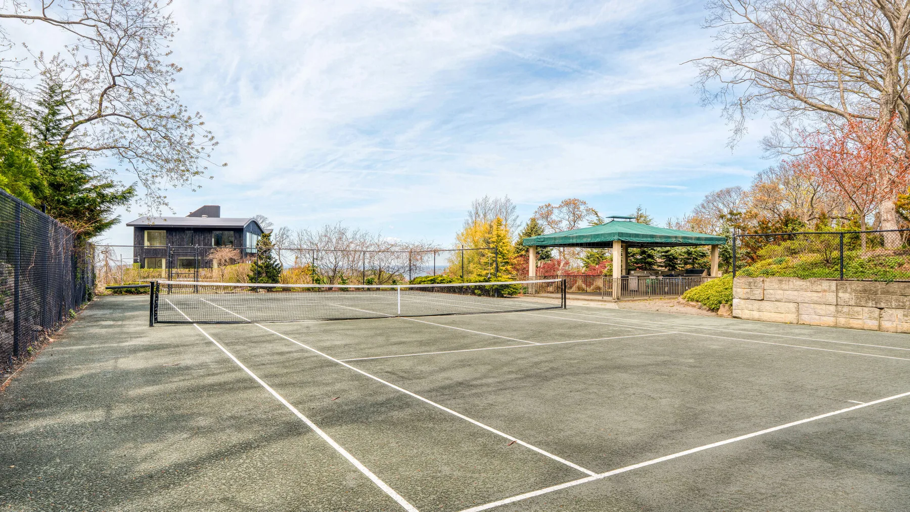 Una pista de tenis al aire libre está rodeada de vallas y árboles.