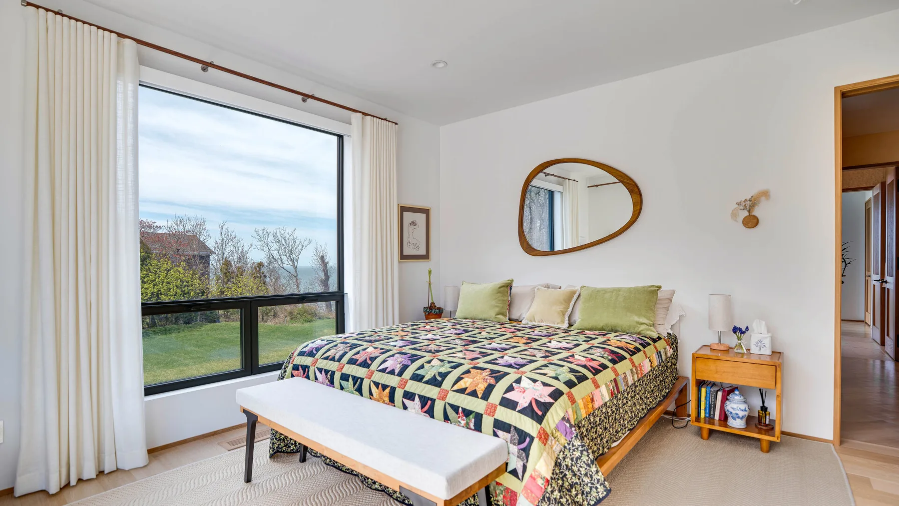 A bright bedroom with a patterned bed beside a large window.