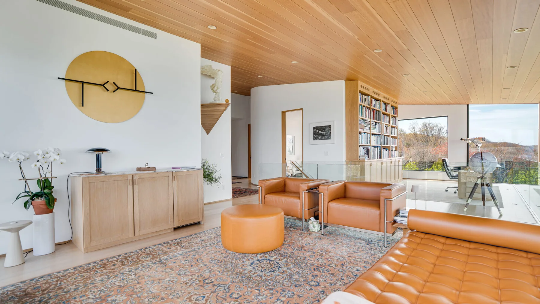 A bright living room with leather seating, a patterned rug, and large windows.