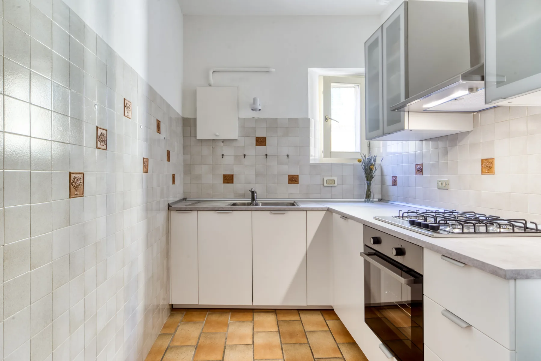 Una cocina luminosa con armarios blancos, paredes de azulejos y una placa de gas.