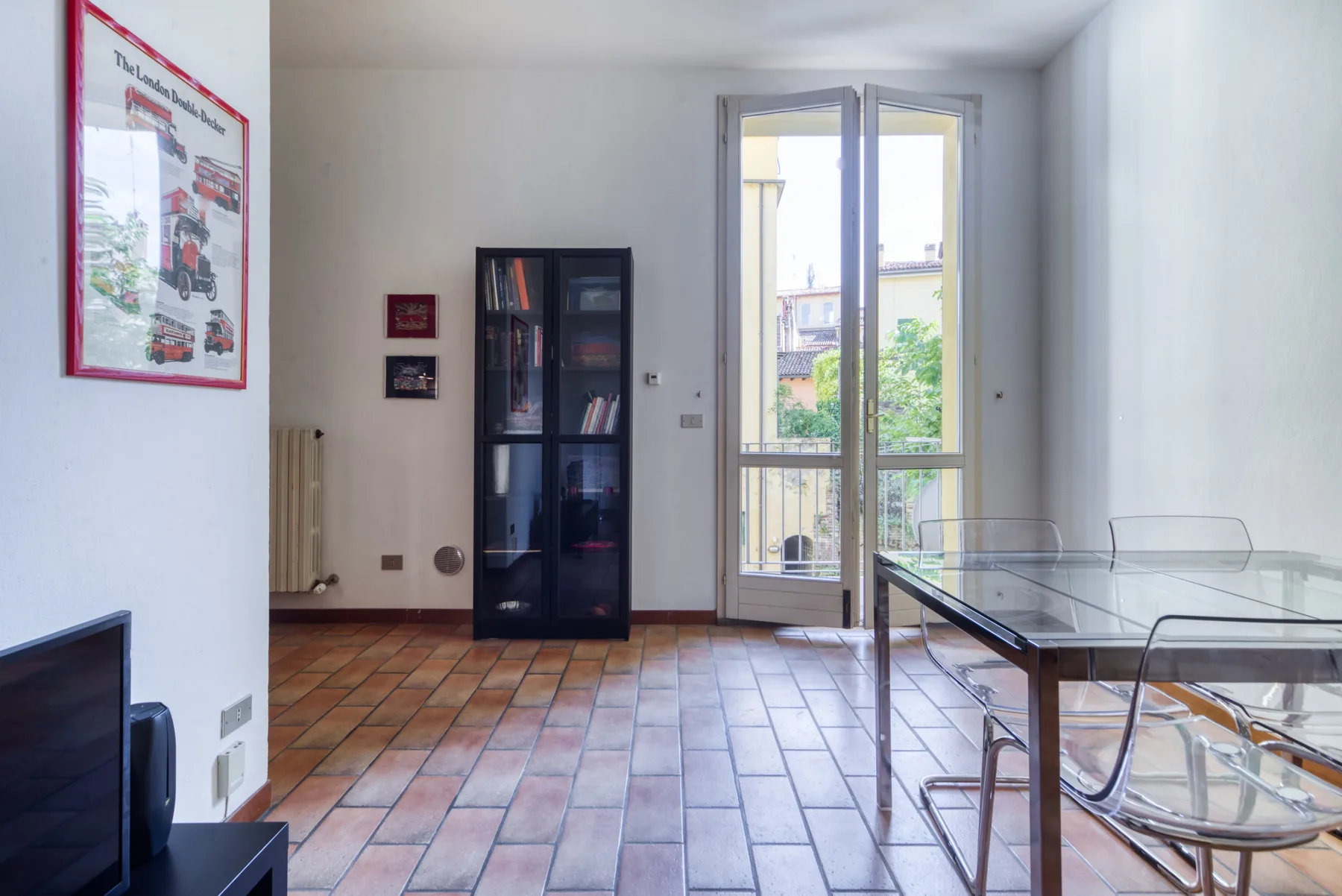 A bright room with a glass dining table, bookcase, and tall windows.