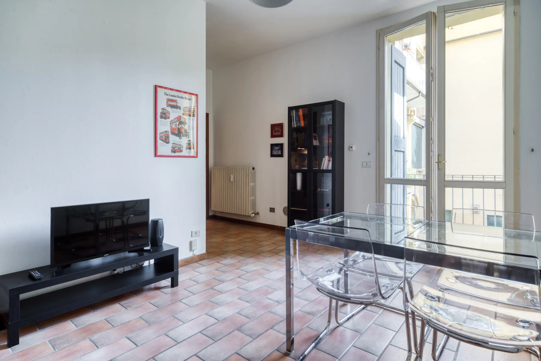 Una luminosa sala de estar y comedor con televisor y mesa de vidrio.