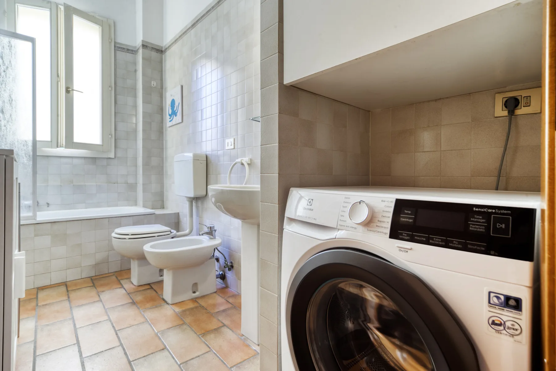 Un baño alicatado con inodoro y lavabo junto a una lavadora de carga frontal.