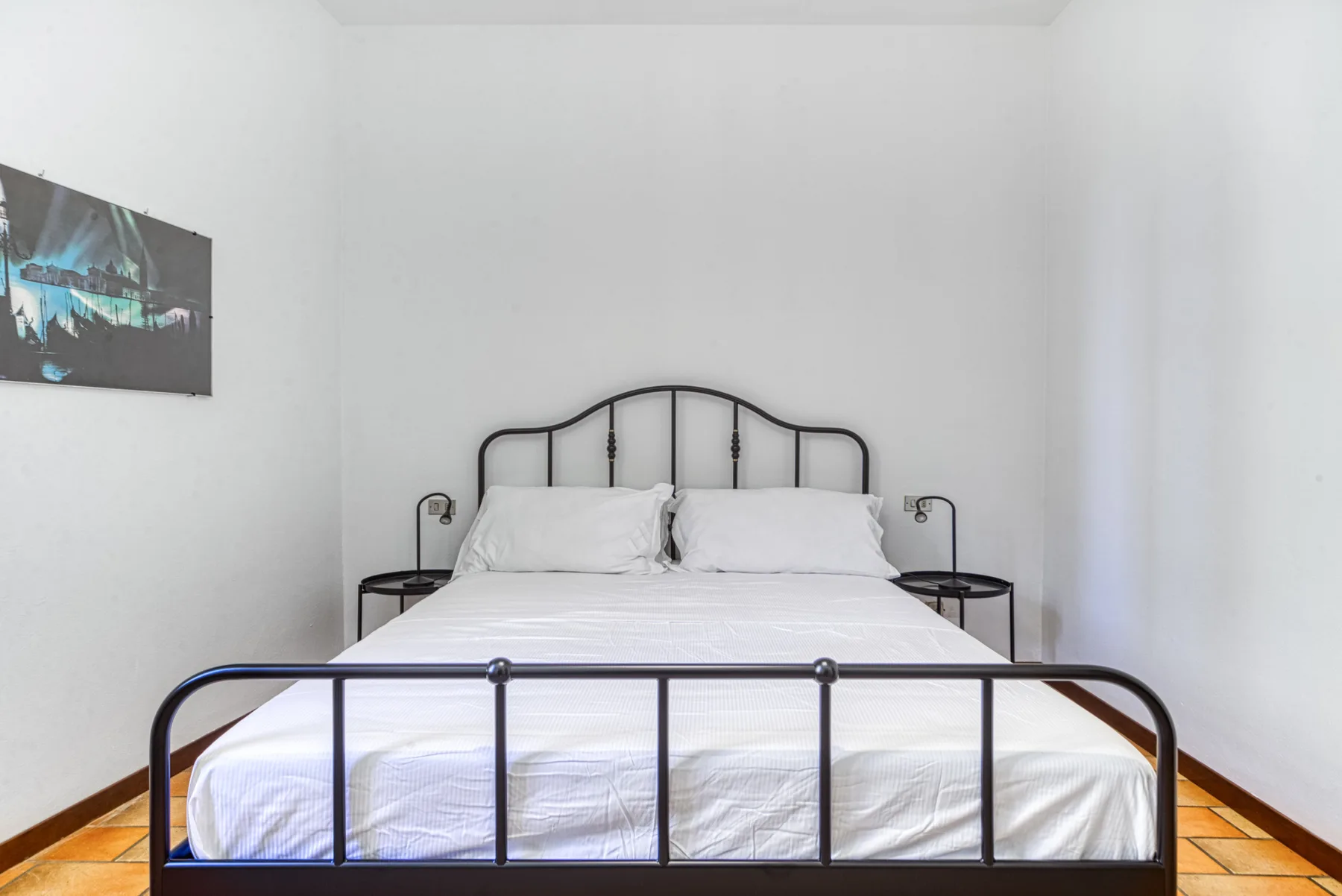 Un dormitorio con una cama vestida con sábanas blancas y un armazón de metal negro.