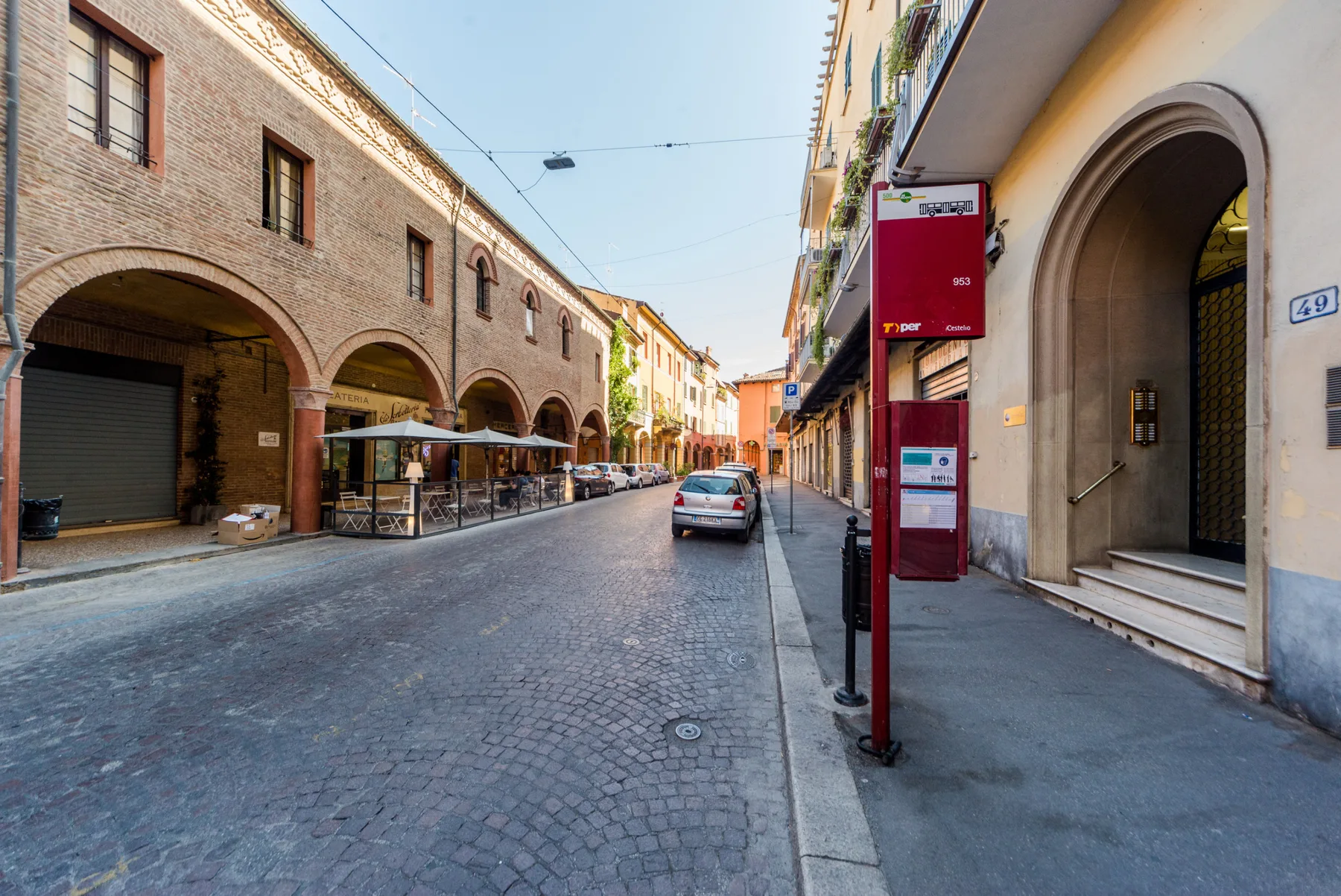 Una calle empedrada flanqueada por edificios de ladrillo, comercios y un automóvil estacionado.