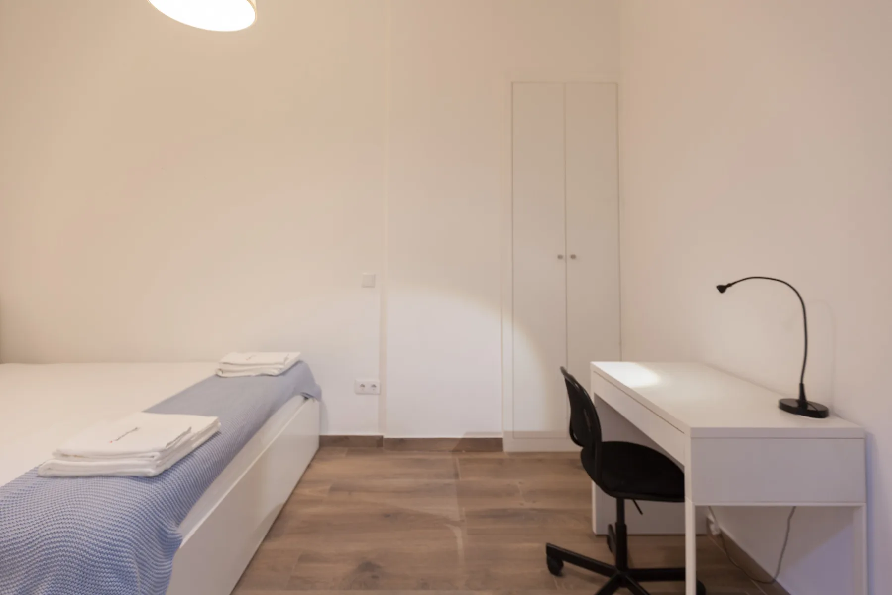 A bedroom with a single bed, wardrobe, and desk.