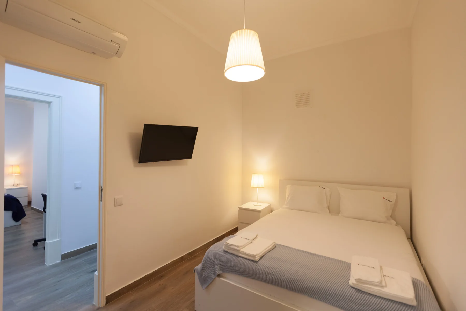 A bedroom with a double bed, folded towels, and a wall-mounted television.
