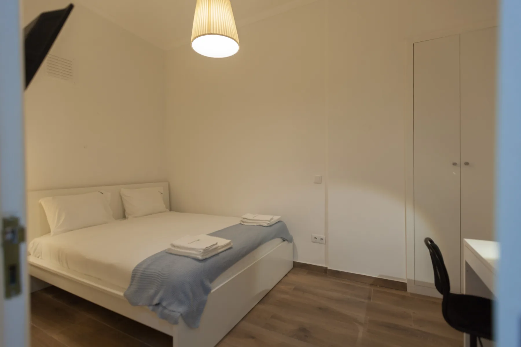 A bedroom with a bed, folded towels, and a wardrobe.