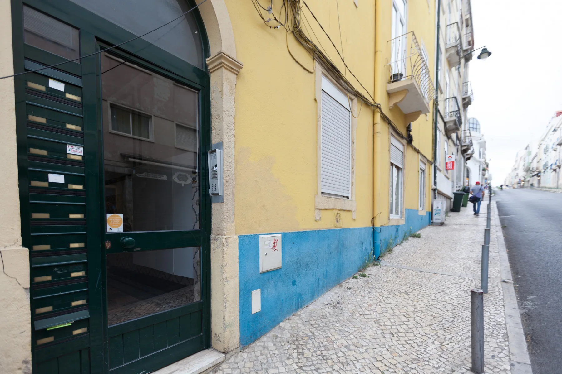 A yellow building entrance opens onto a cobbled sidewalk beside a quiet street.