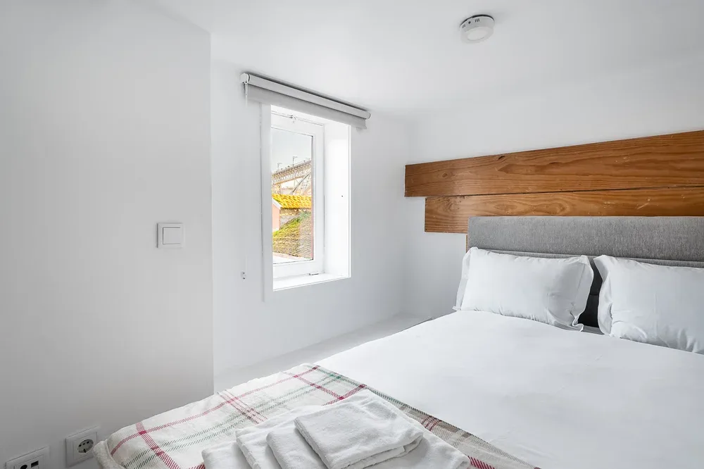 A bright bedroom with a neatly made bed and a window beside it.