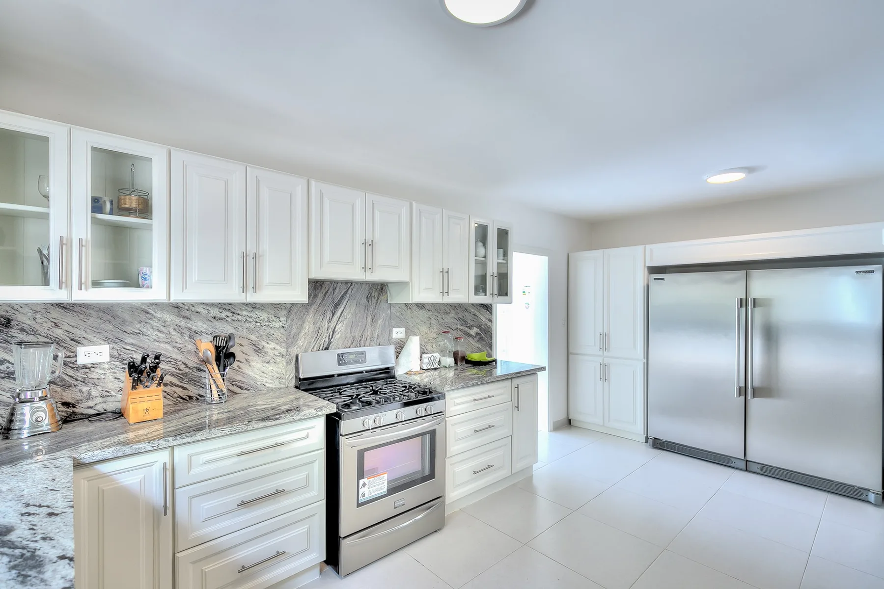 Una cocina luminosa con gabinetes blancos, una estufa y un refrigerador de acero inoxidable.