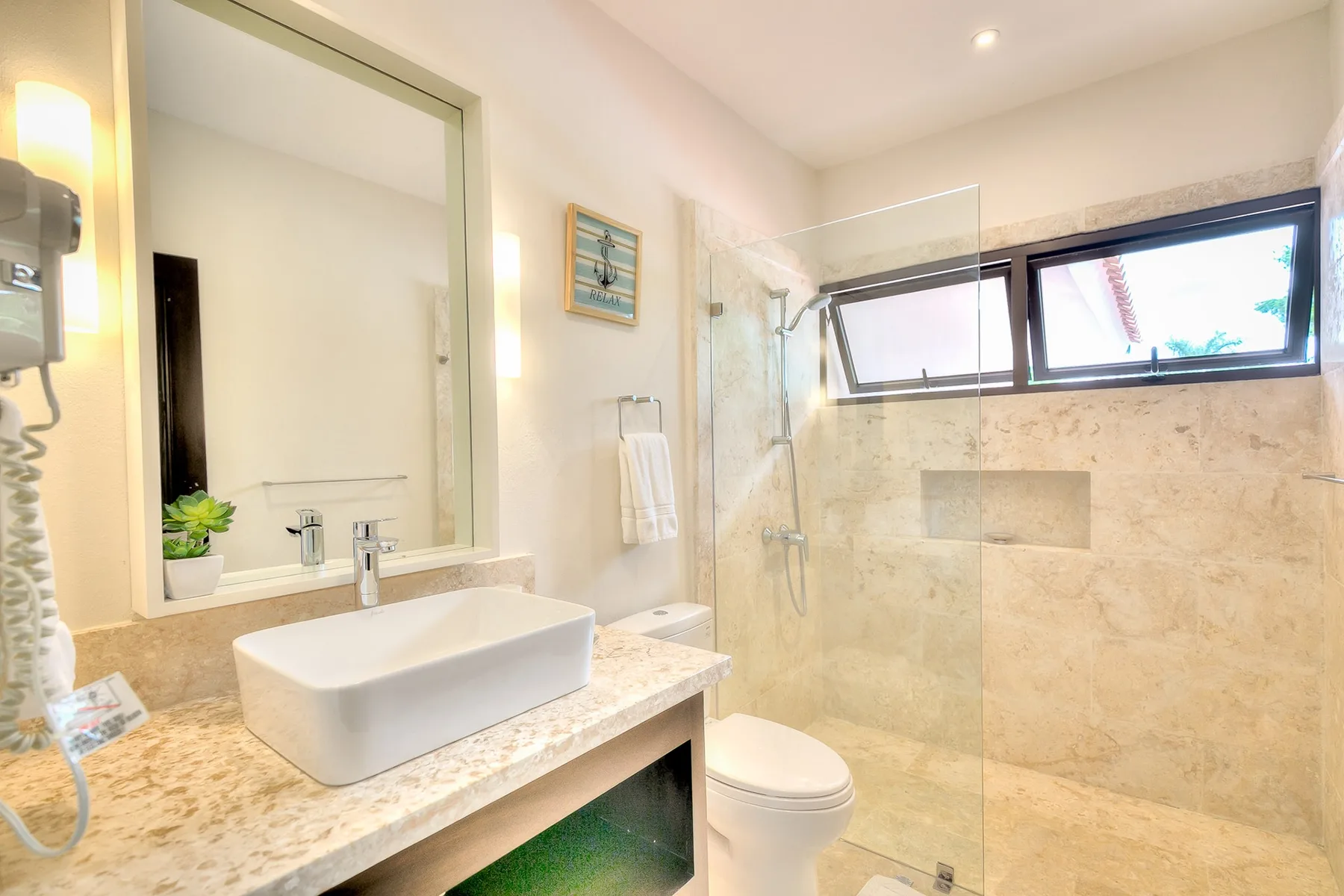 Un baño luminoso con lavabo, inodoro y ducha de vidrio.