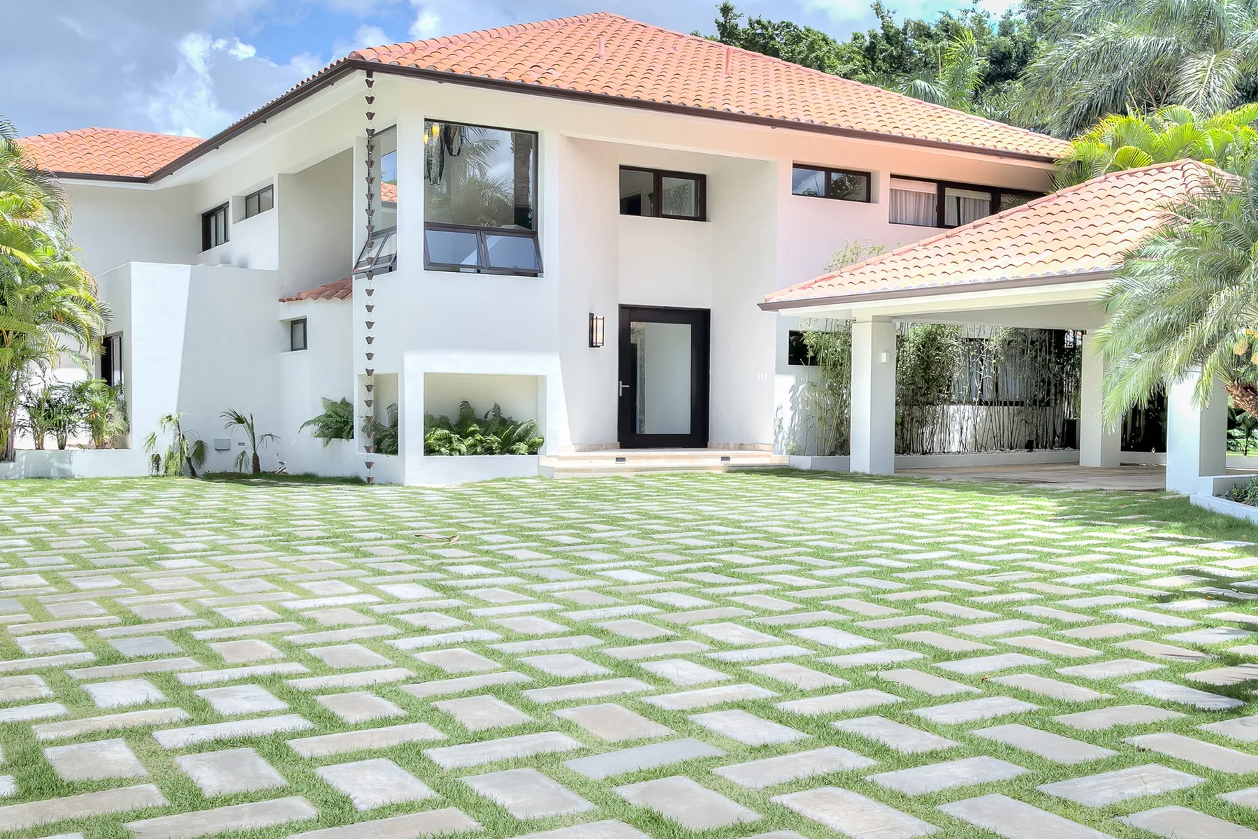 Una gran casa blanca con techos de tejas se alza tras un jardín pavimentado.