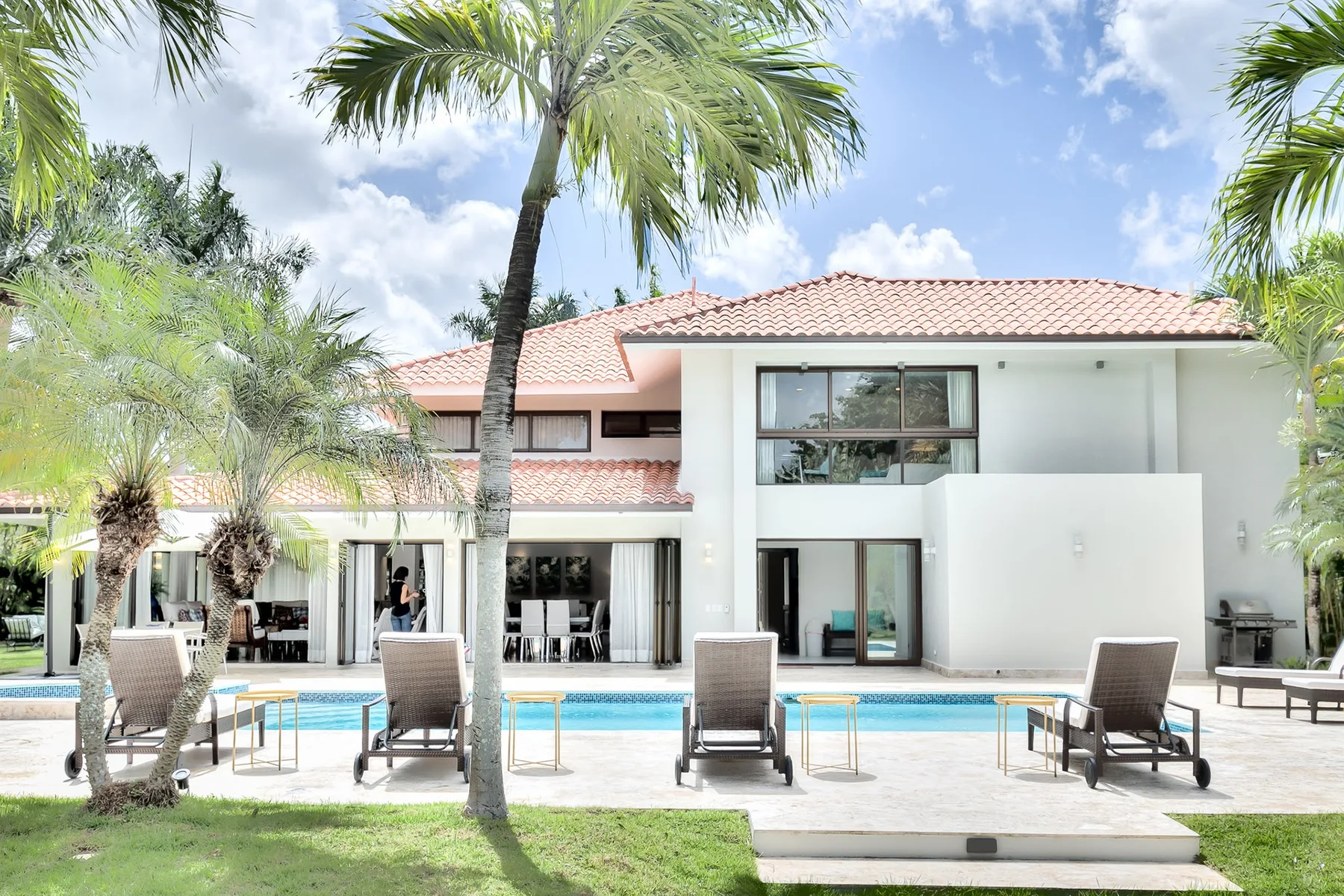 Una casa moderna da a una piscina, con asientos de descanso y palmeras.