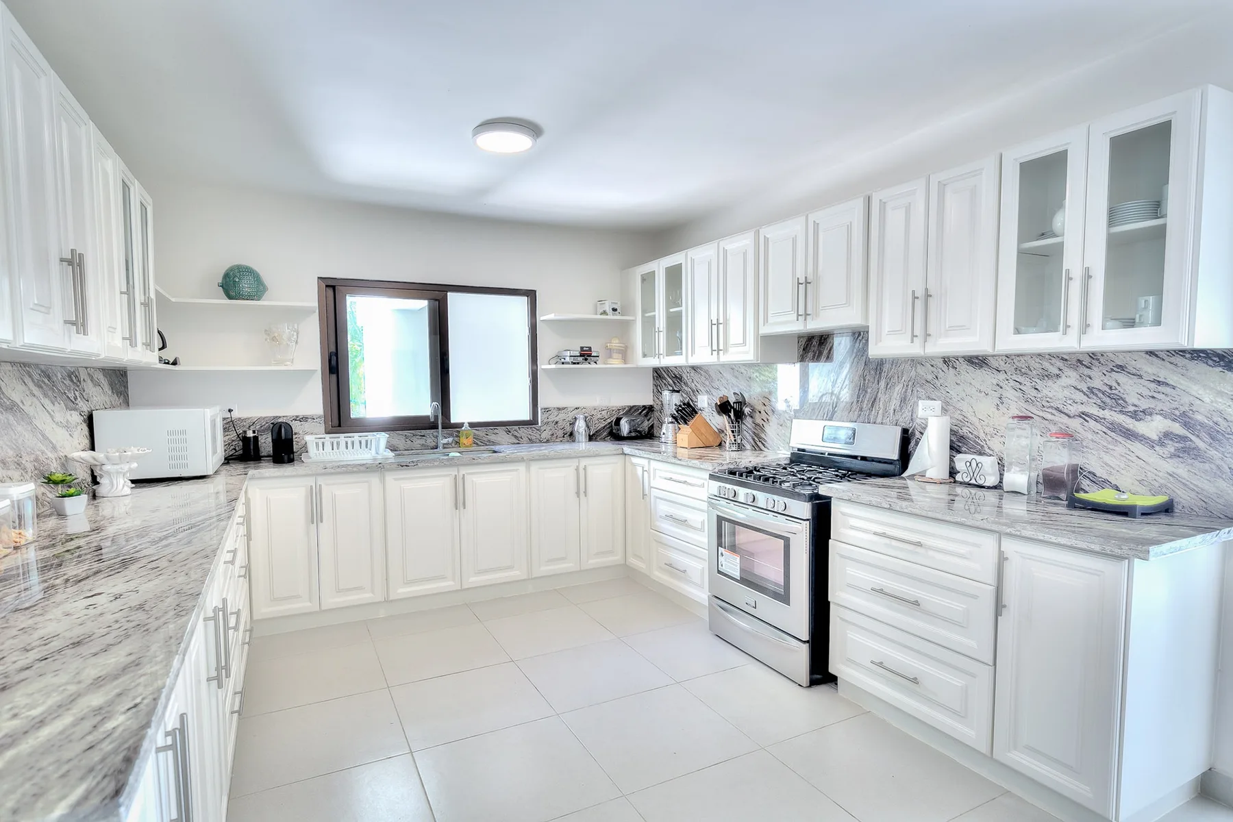 Una cocina luminosa con gabinetes blancos, encimeras de piedra y una ventana sobre el fregadero.