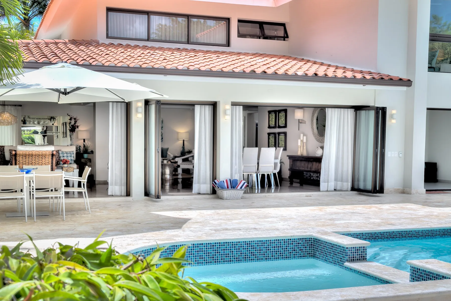 Un patio junto a la piscina da a un edificio con puertas de vidrio abiertas y asientos al aire libre.