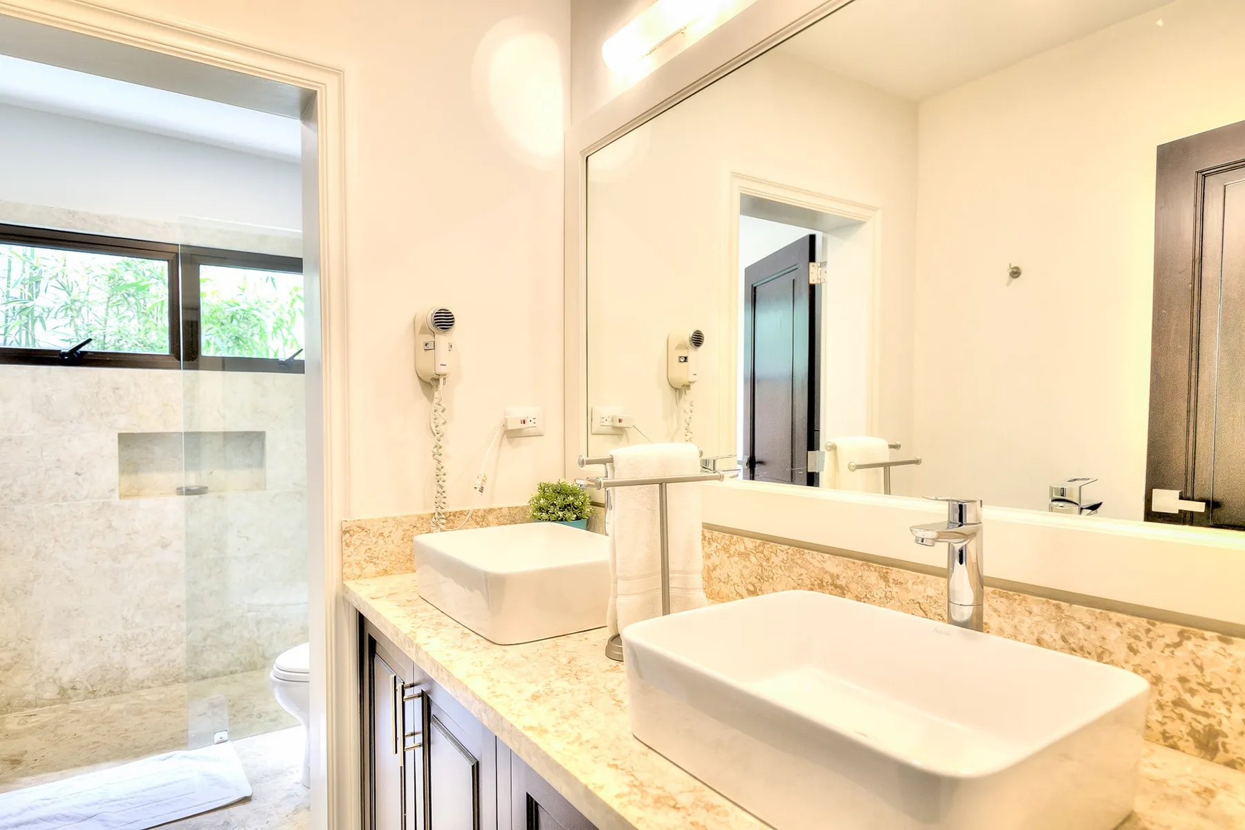 Un baño luminoso con una encimera larga, dos lavabos y un espejo grande.