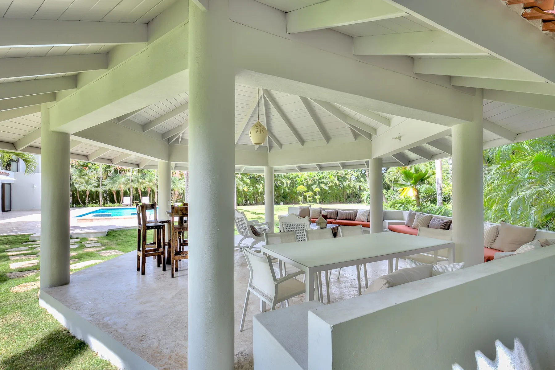 Un patio cubierto y abierto tiene una mesa de comedor y asientos junto a una piscina.