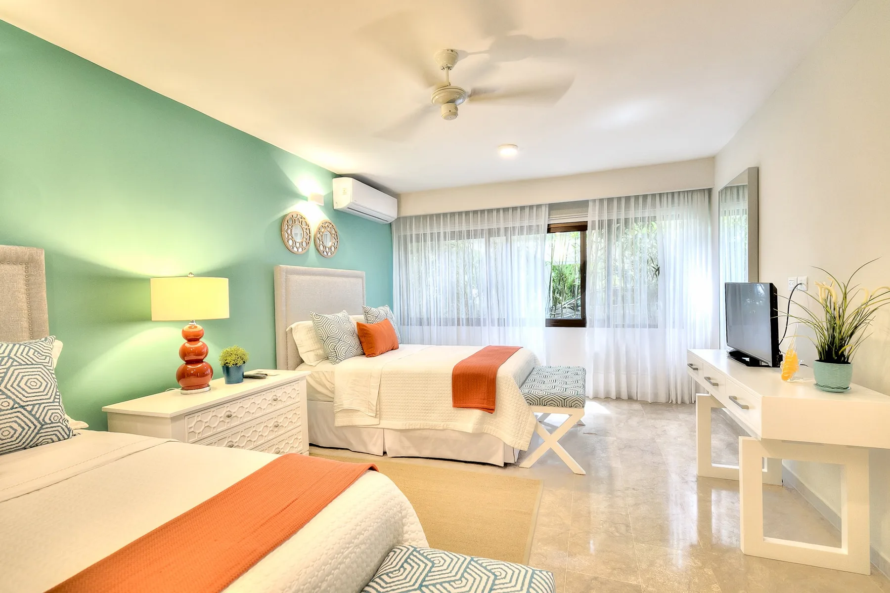 Un dormitorio luminoso con dos camas, una pared verde menta y cortinas translúcidas.