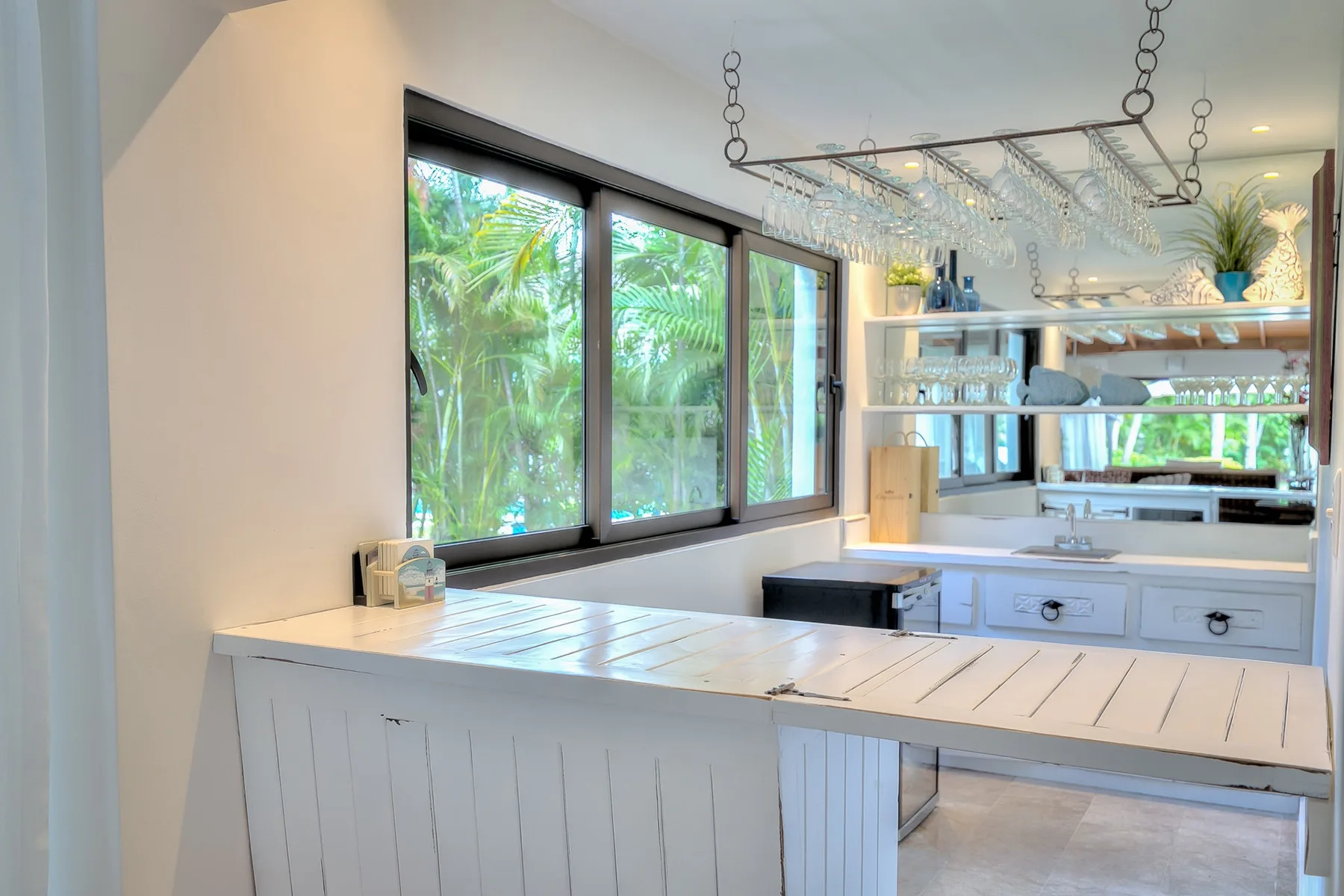 Una cocina luminosa con una barra larga, estantes abiertos y ventanas amplias.