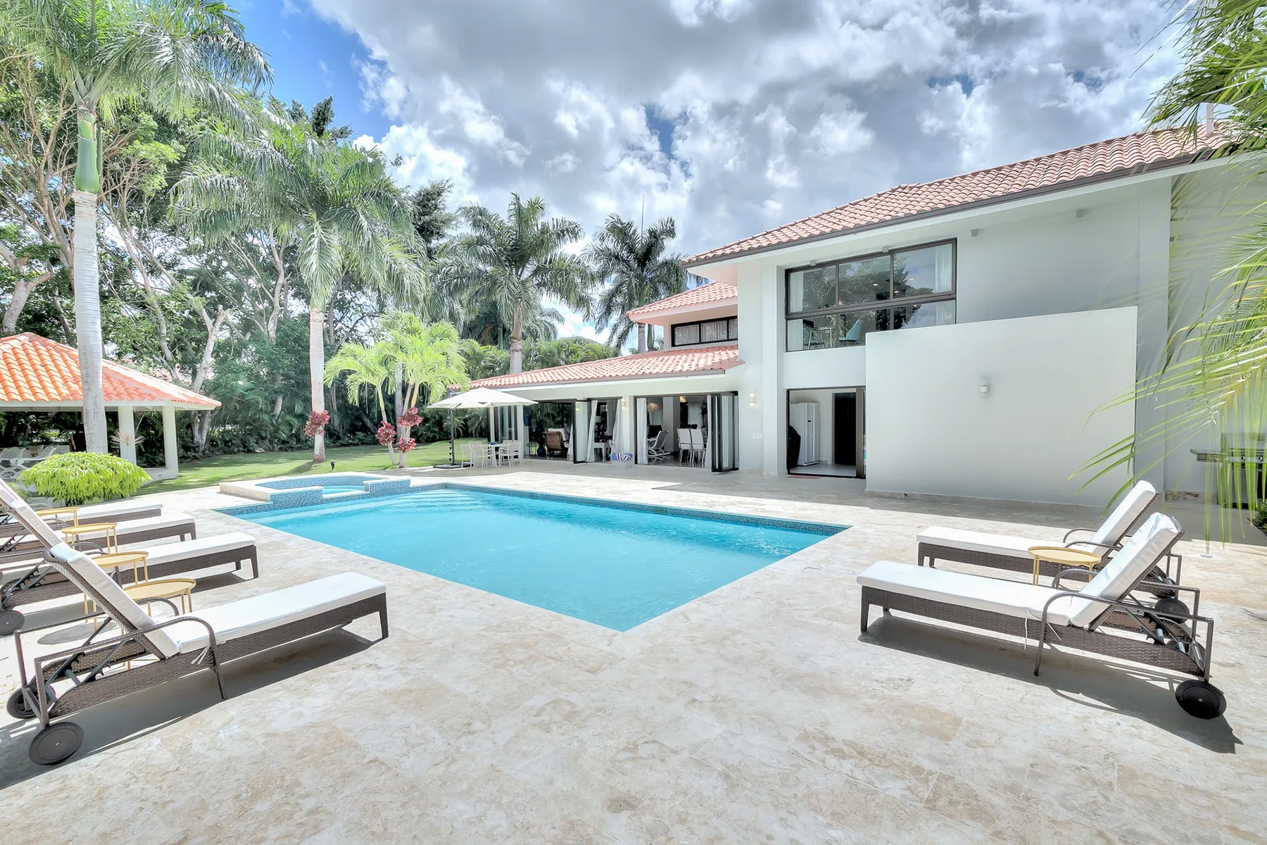 Una piscina y asientos reclinables están junto a una casa blanca moderna.