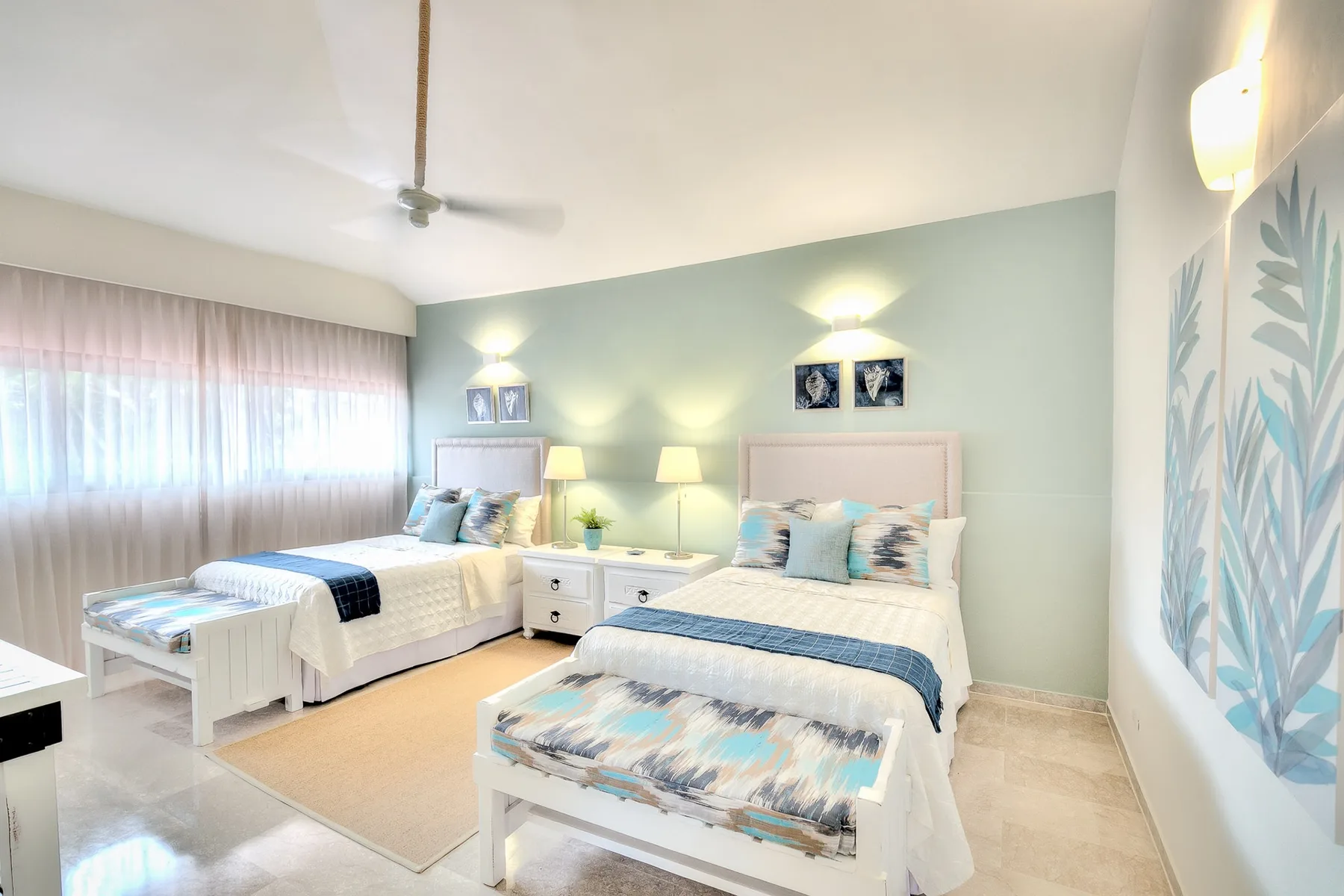 Un dormitorio luminoso con dos camas, mesitas de noche y una gran ventana con cortinas.