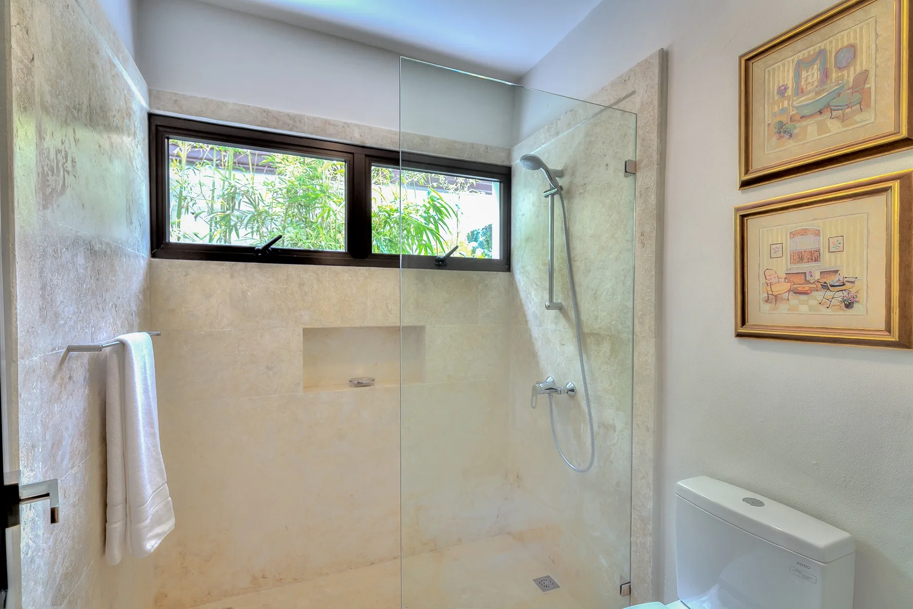 Un baño con ducha, ventanas altas y cuadros enmarcados.