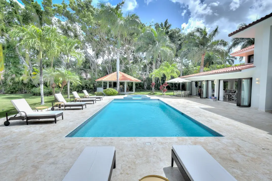 Una piscina al aire libre está junto a un patio y un jardín tropical.