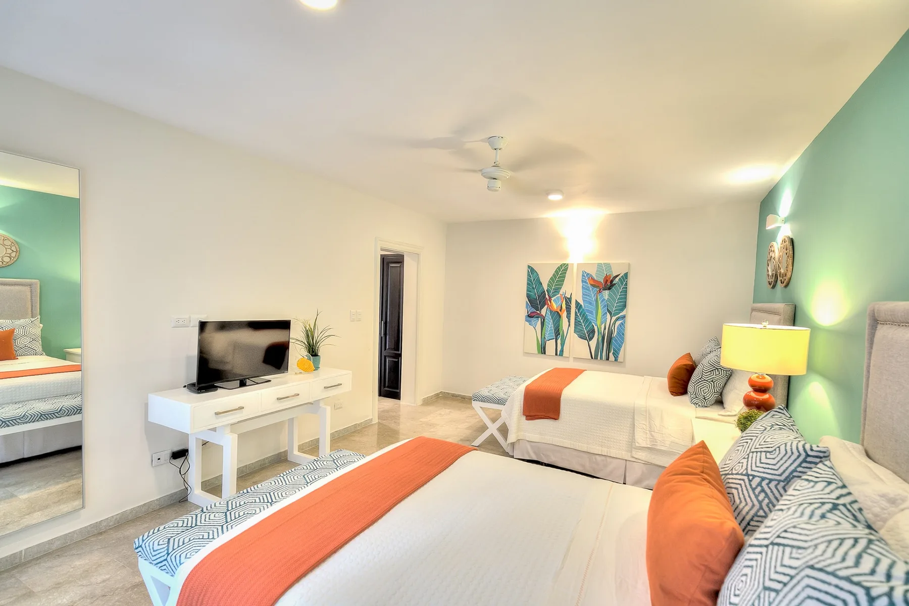 Un dormitorio luminoso con dos camas, un televisor y arte colorido en la pared.