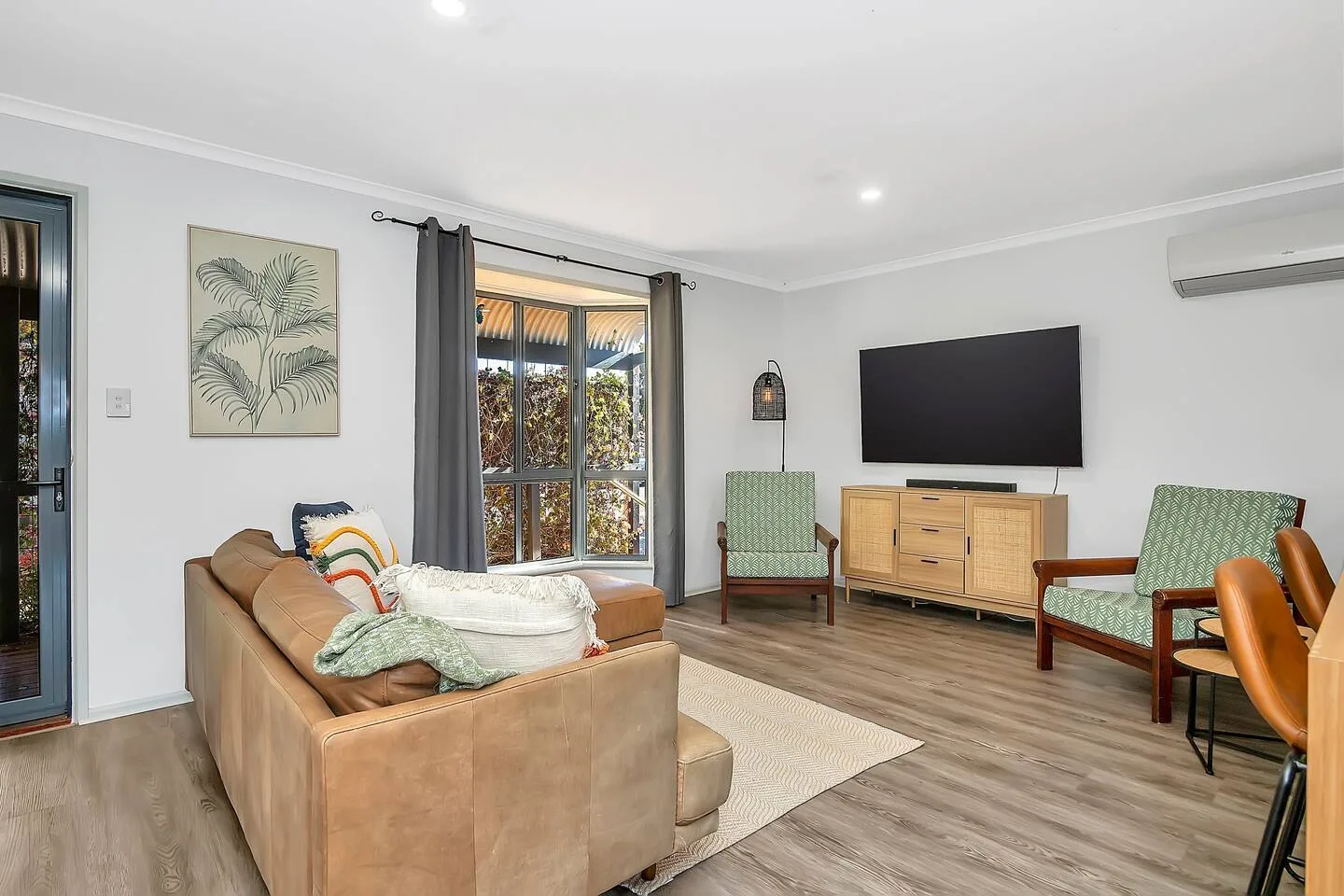 Una sala de estar tiene un sofá, dos sillones, un televisor y un mueble.