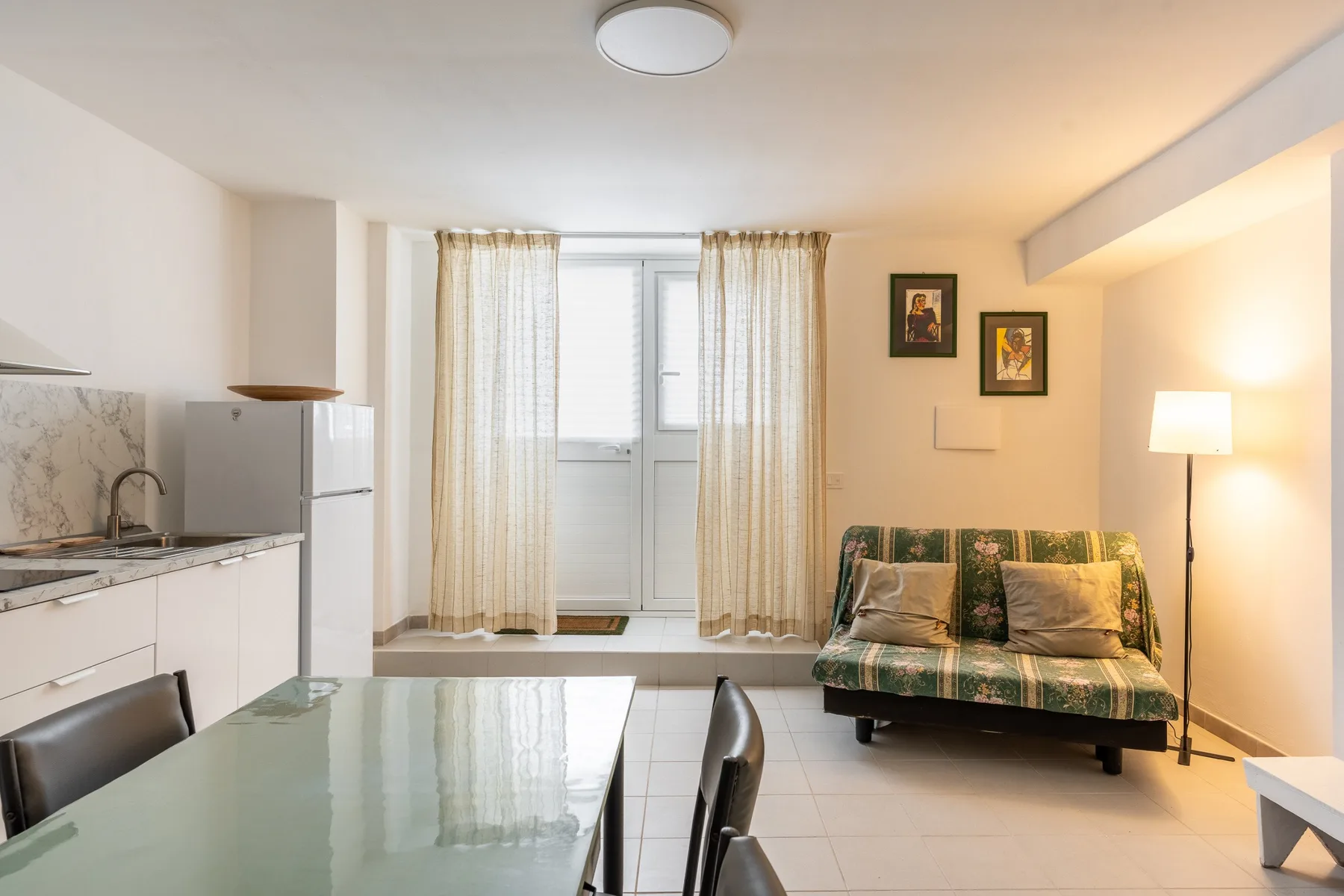 A compact kitchen and dining area with a small green patterned sofa beside the window.