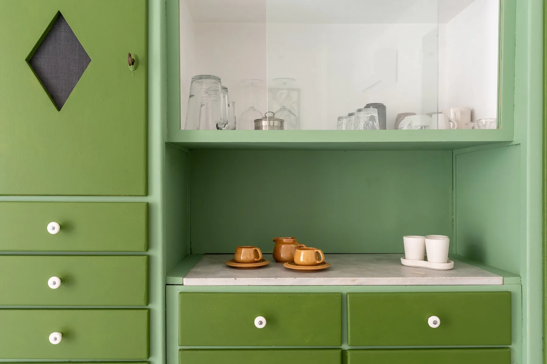 A green built-in cabinet displays cups and glassware on its shelves.