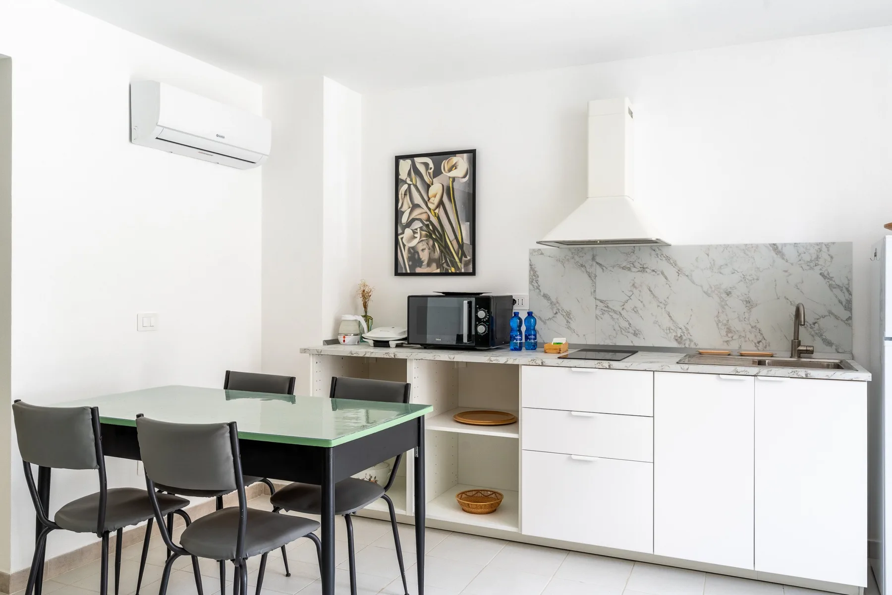 A bright kitchen with white cabinetry and a glass dining table.