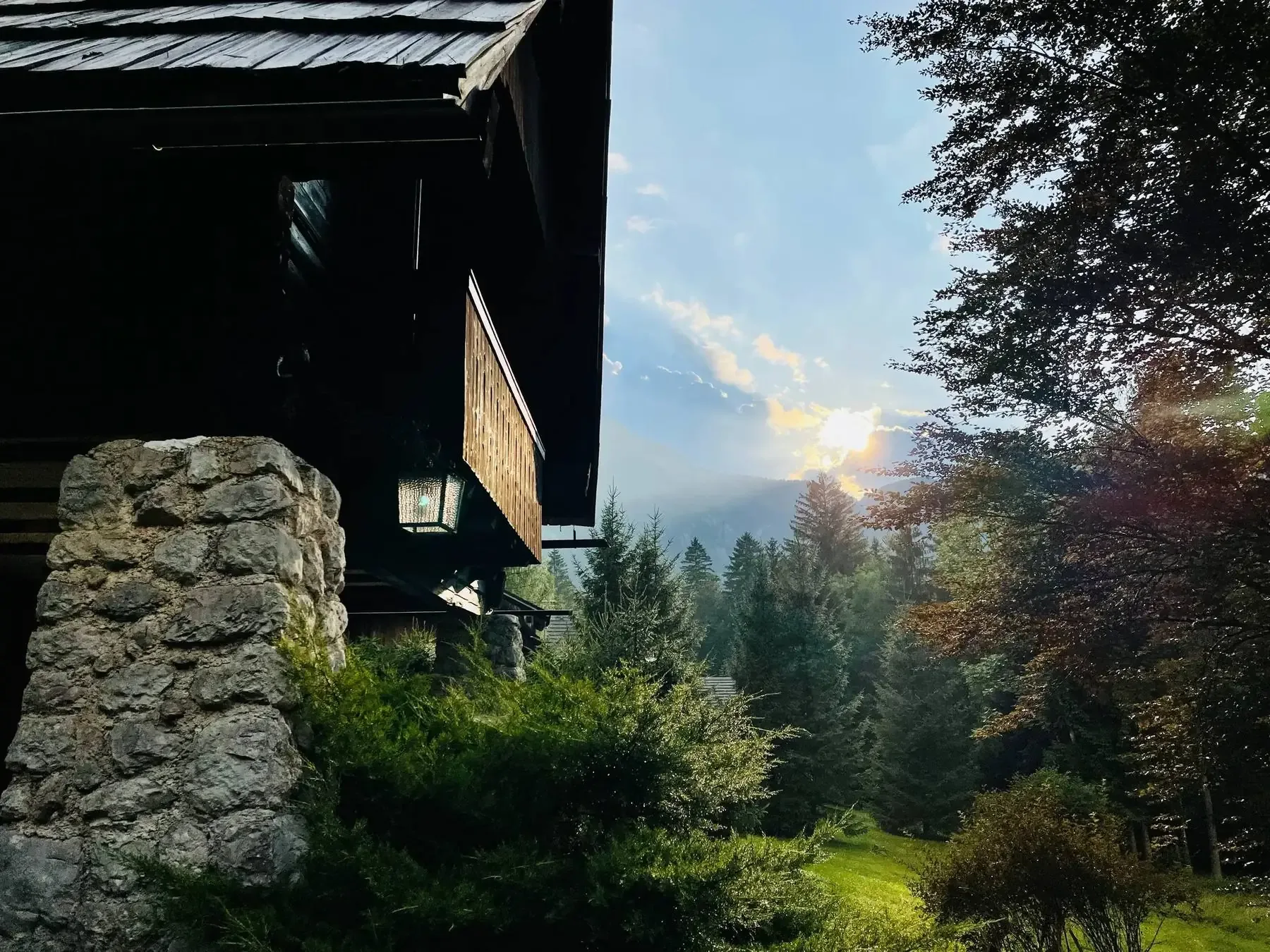 Pilar de piedra y farol de Red Beech Cabin al anochecer, con montañas y bosque al fondo