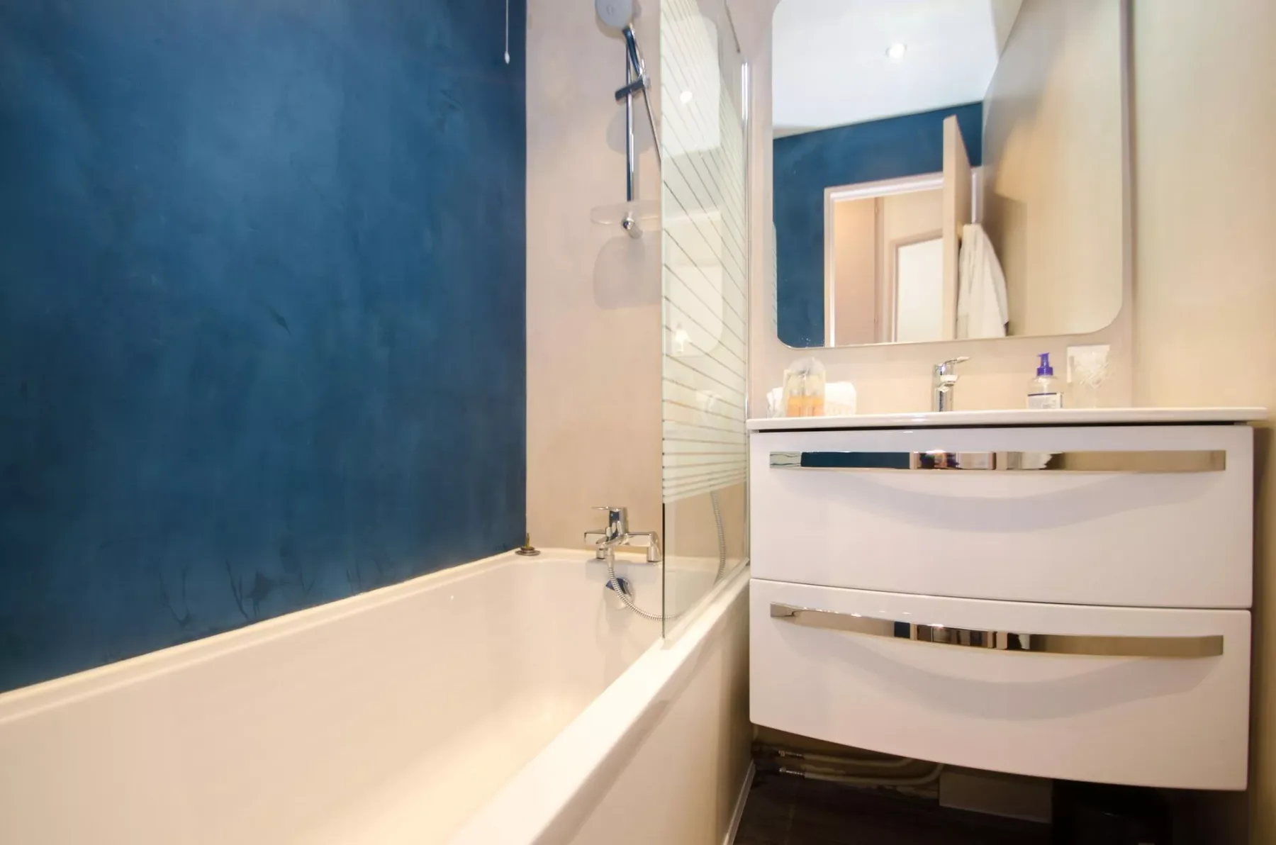 A bathroom with a bathtub, shower fixture, and vanity beneath a mirror.