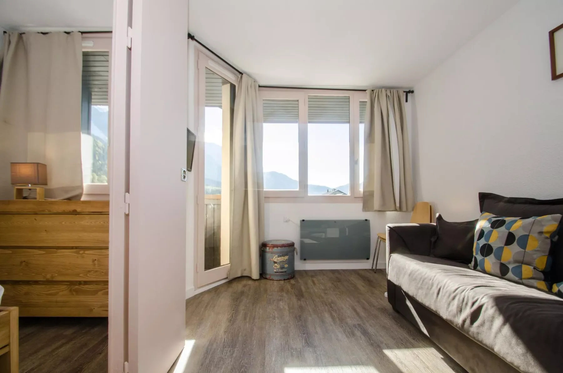 A bright living room with seating beside large windows and light curtains.
